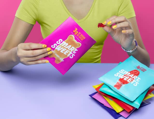 Woman holding Fruity Gummy Bear pouch and pouches on side of table