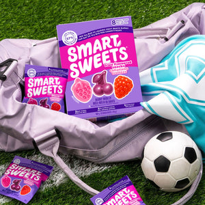 Smart Sweets fruit-flavored gummies packaging on grass with a soccer ball and bag.